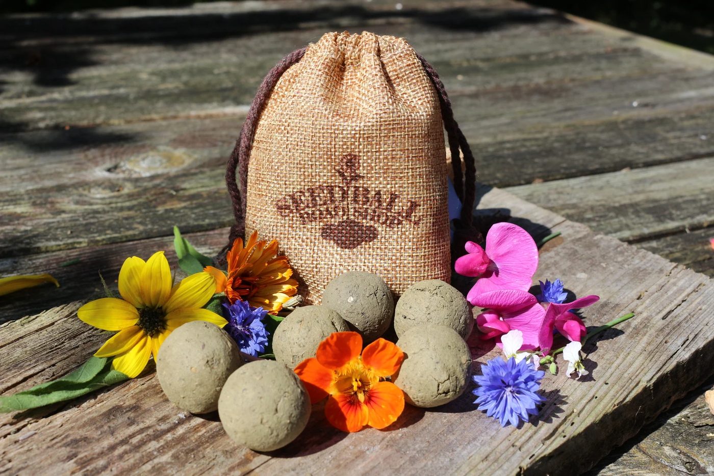 Jute bag with Seedball Roadshop print, surrounded by seed bombs and flowers