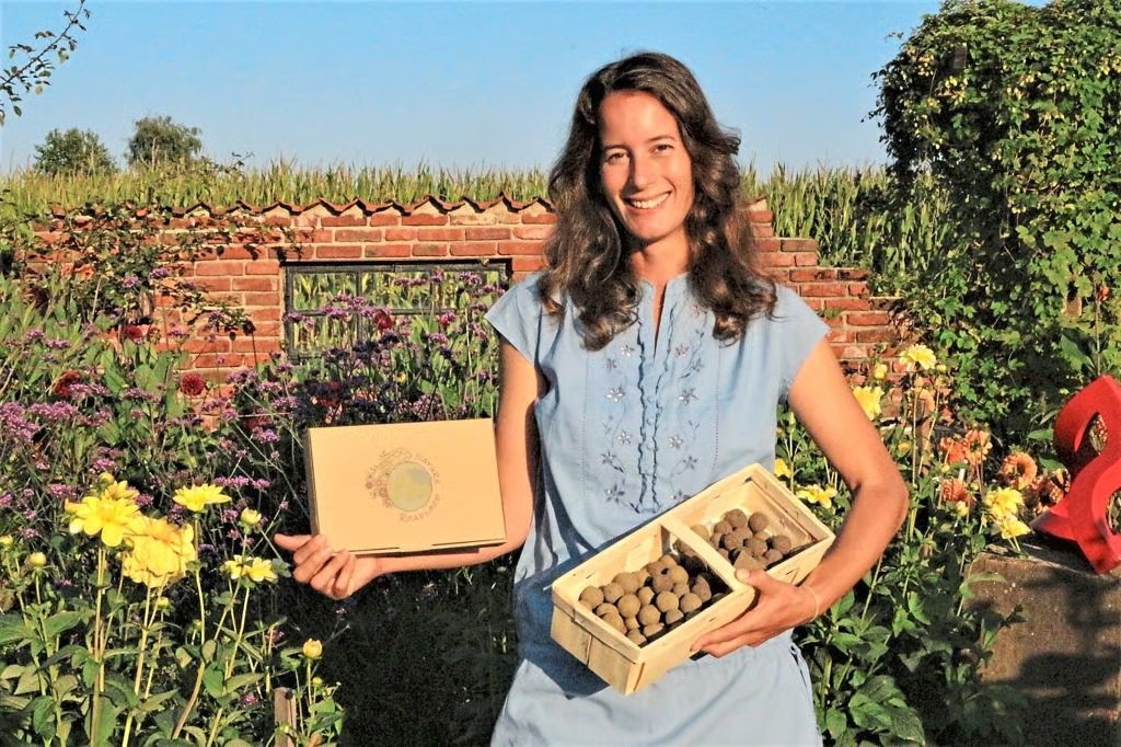 Lena Wildhagen steht in ihrem Blumengarten in Gronau und hält eine Holzkiste voller handgerollter Samenbomben sowie eine Geschenkschachtel